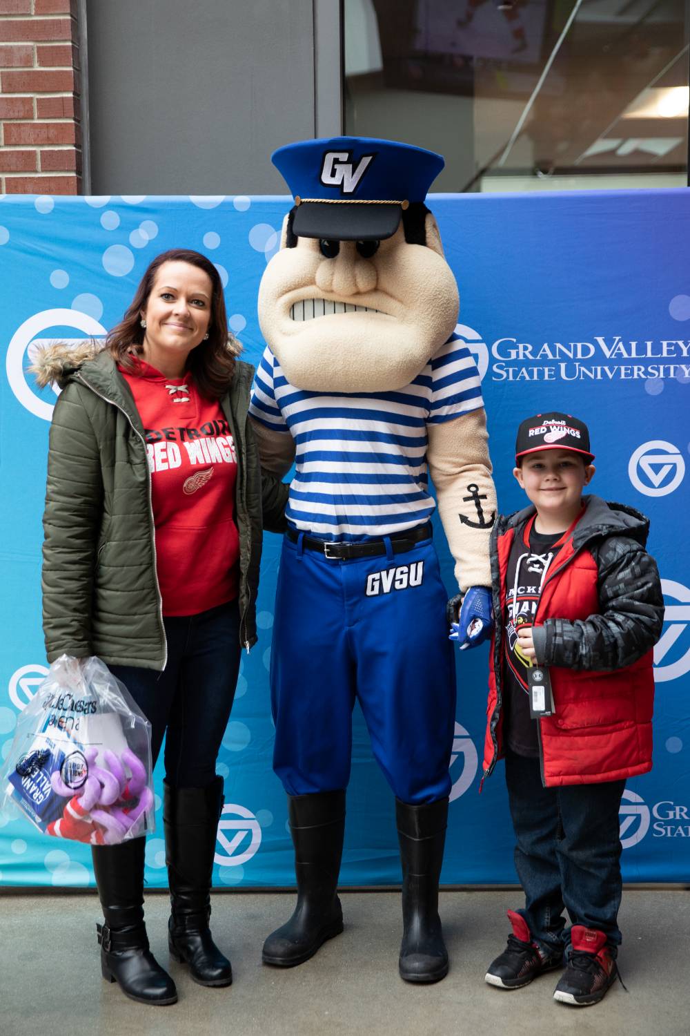 An alumna and her child pose with Louie the Laker at the Detroit Red Wings GVSU Night